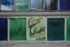 Close up of paints tiles on a staircase that are green and blue. The artists name Catherine winship is carved into one of the tiles.