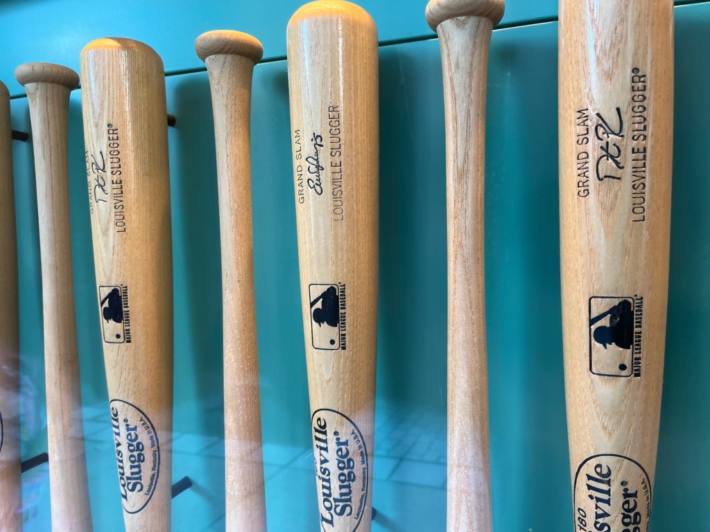 A line of baseball bats on a green backdrop, standing vertically in a storefront window. 