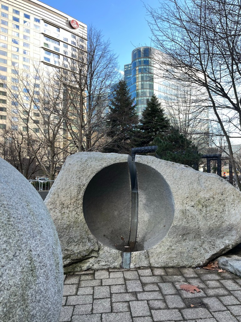 A circular stone sculpture with high rise buildings behind it 