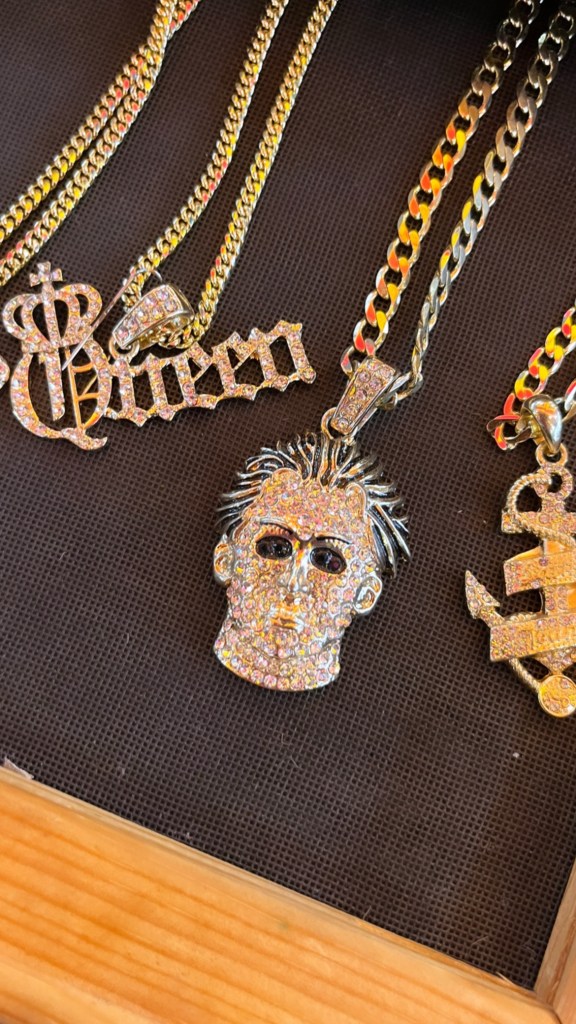 a gold necklace with a charm that is in the shape of a Michael Myers mask.